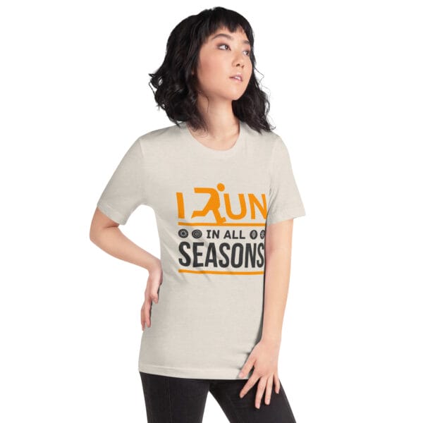 Young woman wearing a heather dust staple t-shirt with text "I run in all seasons" with the letter R a silhouette of a runner