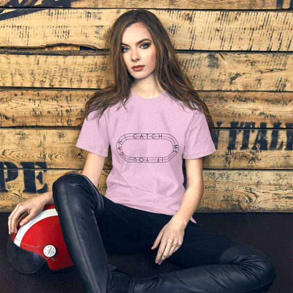 Young woman sitting against wall in a heather prism lilac t-shirt with a black running track with text "Catch me if you can" inside