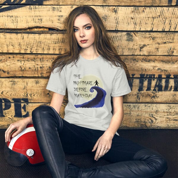 Young woman sat against a wall wearing staple t-shirt in silver with Cristiano Ronaldo 'Sui' celebration and text "The nightmare before matchday"