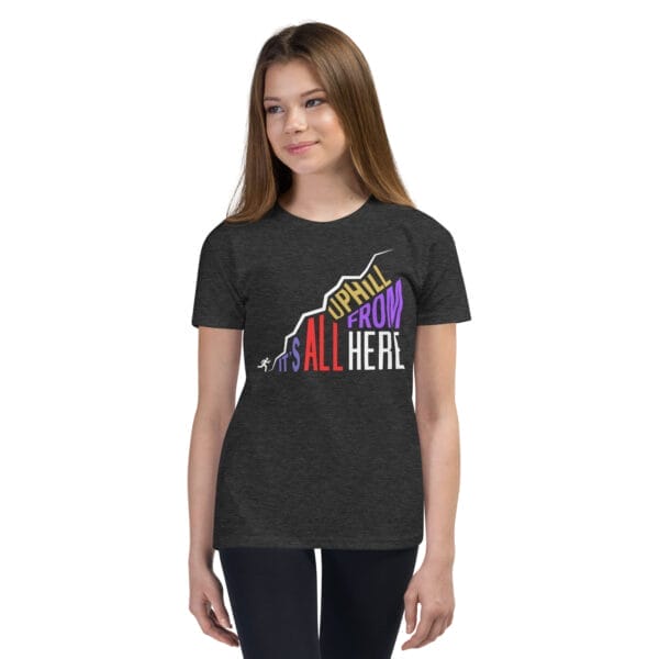 Young girl wearing a dark grey heather staple t-shirt with text "It's all uphill from here" in shape of a hill