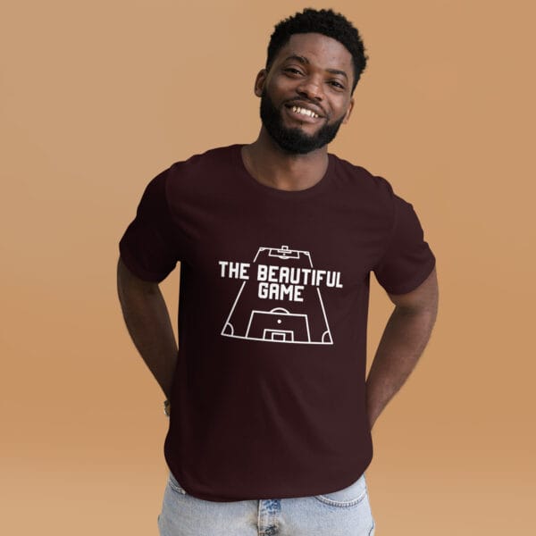 Man wearing a staple t-shirt in oxblood black with white text 'The Beautiful Game' inside a football pitch