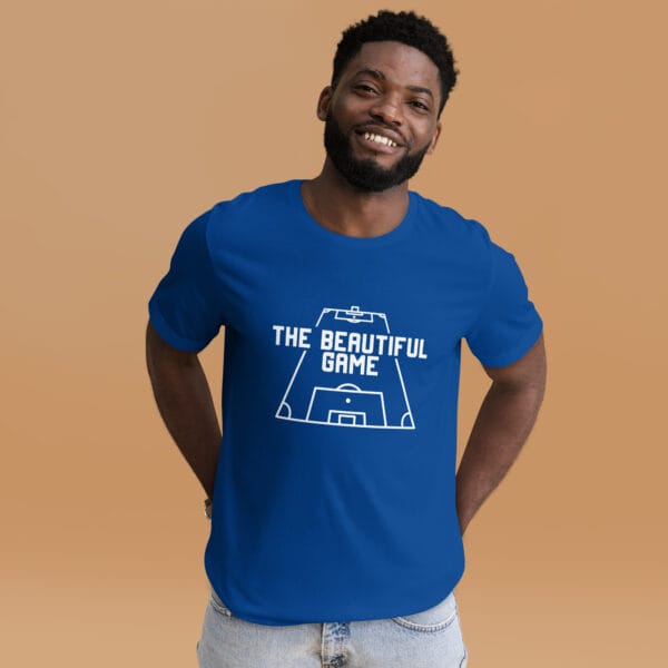 Man wearing a staple t-shirt in true royal with white text 'The Beautiful Game' inside a football pitch