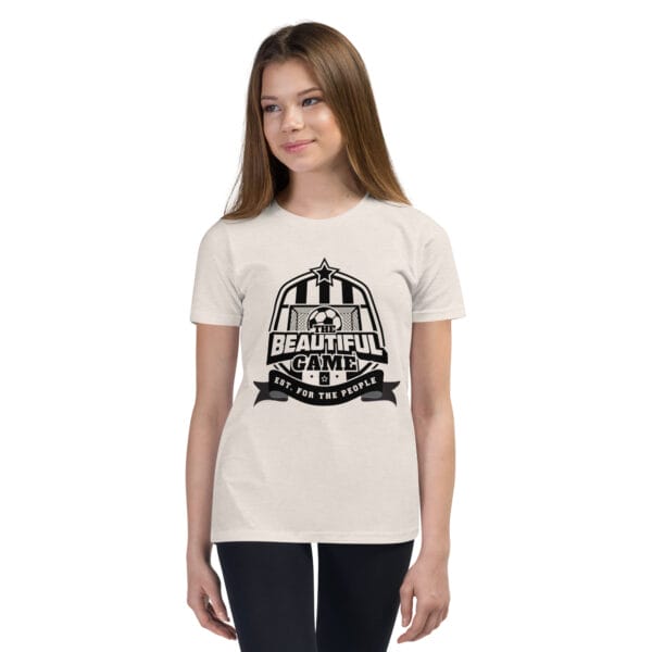 Girl in a heather dust staple t-shirt with a black The Beautiful Game crest, est. for the people