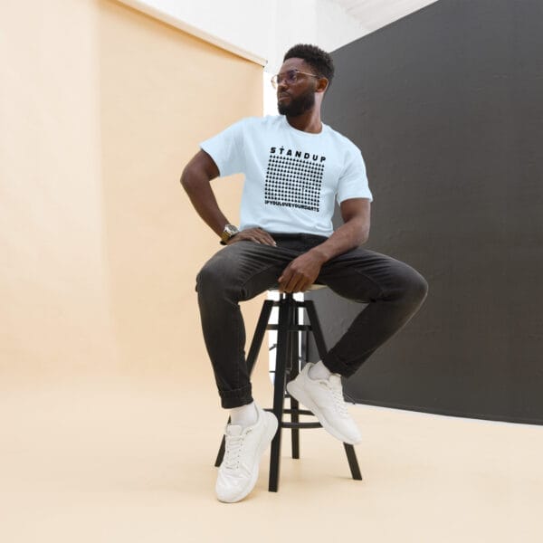 Man sitting on a chair in classic tee in light blue with text 'Stand up if your love your darts' with one icon from many standing