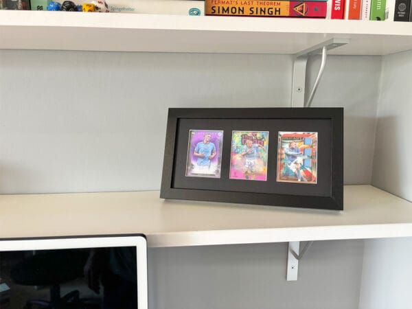 Erling Haaland memorabilia display on a shelf, black frame holding three sports cards, with Haaland autograph