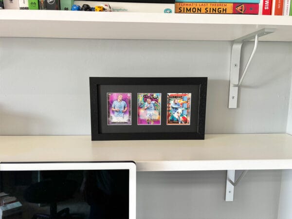 Erling Haaland autograph and relic display on a shelf, black frame holding three sports cards