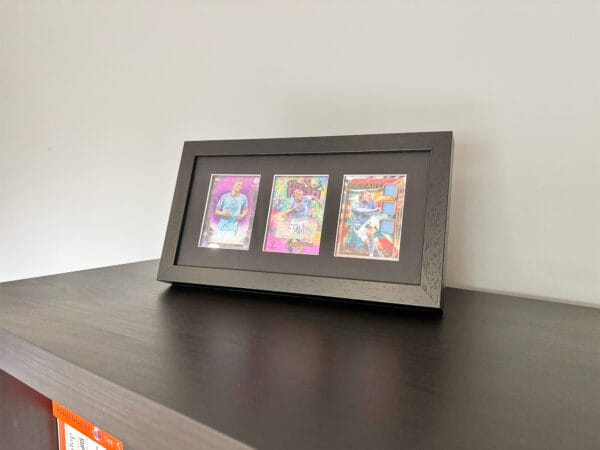 Erling Haaland memorabilia standing using optional leg stand, black frame holding three sports cards, with Haaland autograph